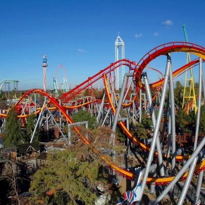 The image shows a large amusement park with multiple colorful roller coasters, loops, and various thrill rides set against a clear blue sky.
