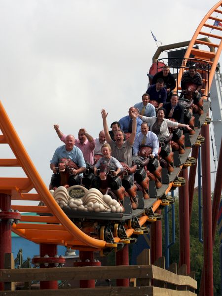 A group of people are riding a roller coaster, appearing excited with their hands raised as the ride descends on the track.
